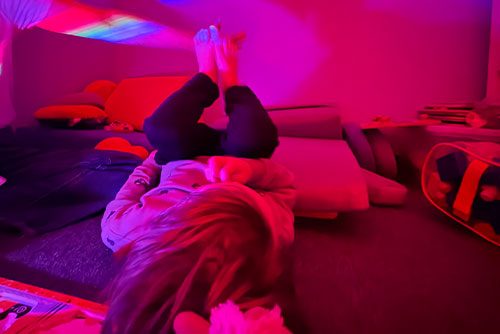 Child lying down in a softly red and pink lit room, illustrating sensory rest and self-regulation supported in neurodiverse affirming speech therapy in NYC.