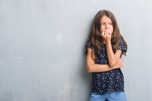 Young hispanic kid over grunge grey wall looking stressed and nervous with hands on mouth biting nails. Anxiety problem.