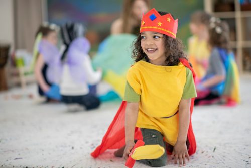 Child engaged in dress-up play with classmates in the background, illustrating creative language and social development supported through speech therapy for autistic children in NYC.
