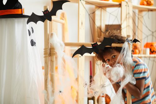 Emotional Afro-American boy with curly hair using cotton wool while making Halloween decoration at home