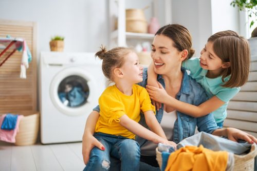 Beautiful young woman and child girl little helper are having fun and smiling while doing laundry at home.