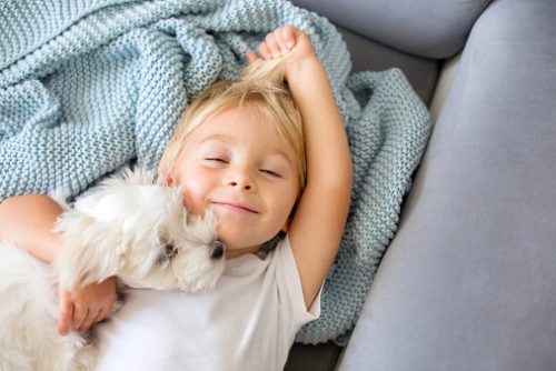Child lying on a couch next to a small white dog and smiling, illustrating calm, comfort, and nervous system regulation supported in neurodivergent speech therapist in NYC practices.