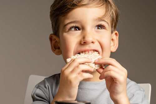 Close up portrait of small caucasian boy four years old eating Crispy puffed rice cake looking to the side - healthy gluten free vegan or vegetarian food - front view studio shot