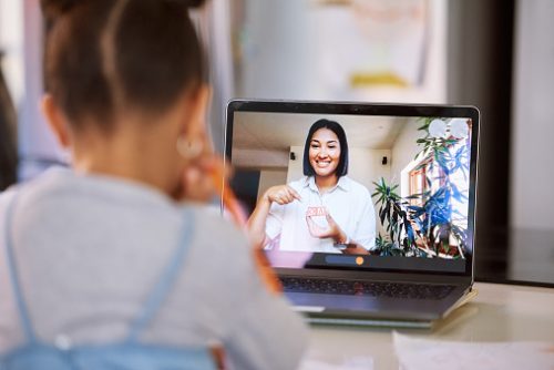 Young child attends an online lesson with a smiling teacher on a laptop screen, illustrating how digital learning influences speech and language development, highlighted by a pediatric speech therapist in NYC.