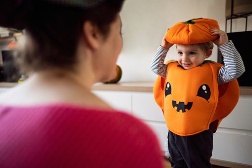 Cute Caucasian toddler boy dressed as a pumpkin, for a Halloween, playing with his mother