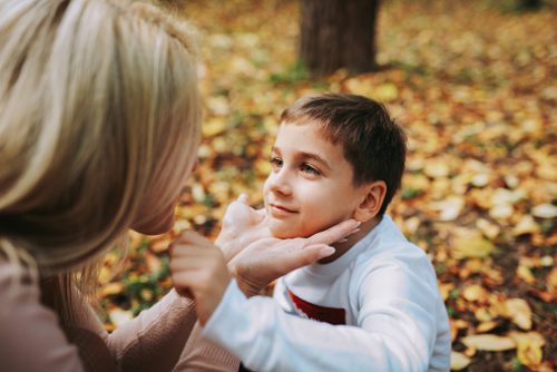 A mother gently holding her autistic child’s face while they connect outdoors on a blanket of fall leaves, symbolizing the warmth and encouragement found through speech therapy for autism in NYC.