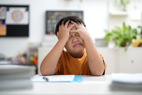 A child sitting at a desk with eyes closed and hands on their forehead, showing signs of struggle that may benefit from pediatric speech therapy in NYC.