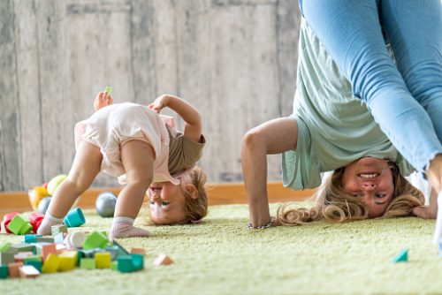 Happy mother and her little daughter standing upside down on the carpet at home