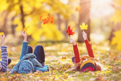 Children lying on the grass with maple leaves in their hands in autumnal park. Concept of the leisure in nature.
