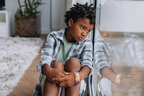 Child sitting by a window with a thoughtful expression, representing the social and emotional impact of screen time on communication, explored by a pediatric speech therapist in NYC.