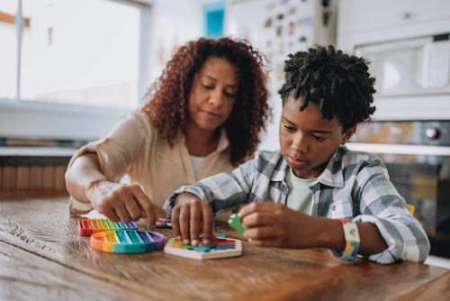 A clinician supporting an autistic child during a hands-on activity at a table, illustrating how speech therapy for autism in NYC helps kids build communication and motor skills.