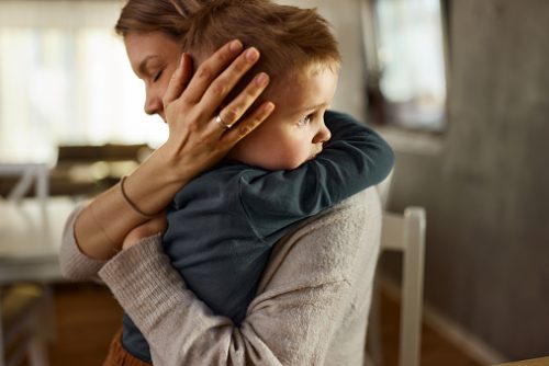 Single mother consoling her sad little boy at home.