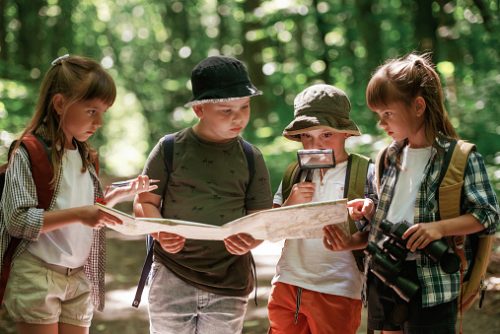 Four children using a map and magnifying glass during outdoor play, showing how face-to-face exploration contrasts with screen-based learning, a concern for a pediatric speech therapist in NYC.