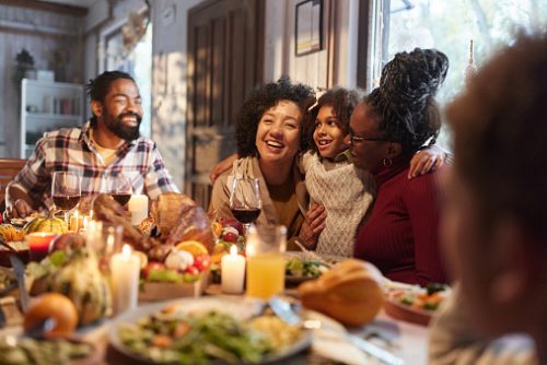 Happy African American girl embracing her mother and grandmother during family's Thanksgiving meal at dining table.