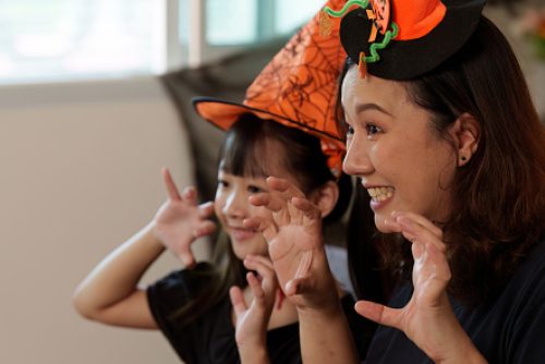 A joyful moment between a mother and daughter during Halloween, showcasing playful gestures and festive hats in a cozy indoor setting.