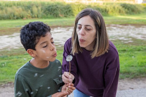 Mother and son sharing a playful moment blowing a dandelion together in nature.