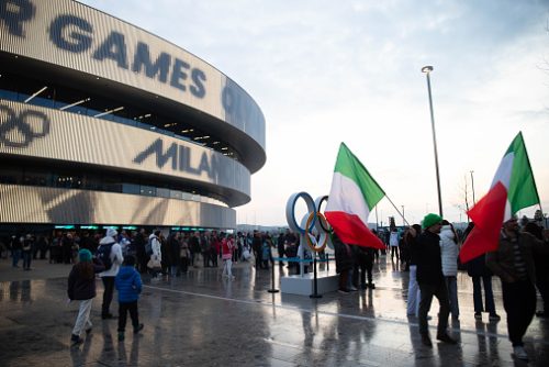 MILAN, FEBRUARY 5th 2026 - People with italian flags outside Arena Santa Giulia during the Milano Cortina 2026 Olympic Winter Games in Milan. Background with copy space at sunset.
