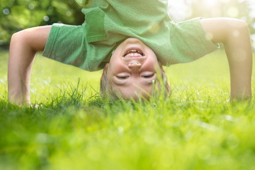 Child standing on their head and smiling upside down, illustrating playful body awareness encouraged in sensory regulation therapy in NYC.