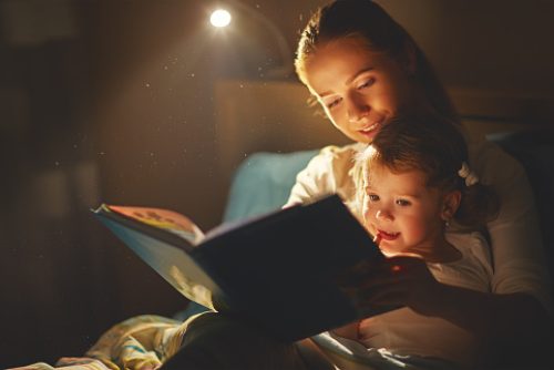 mother and child girl reading a book in bed before going to sleep