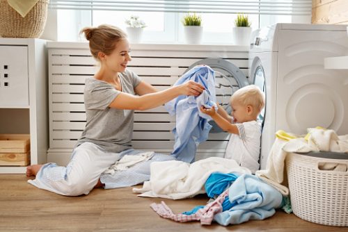 Happy family mother  housewife and child baby son in the laundry load a washing machine