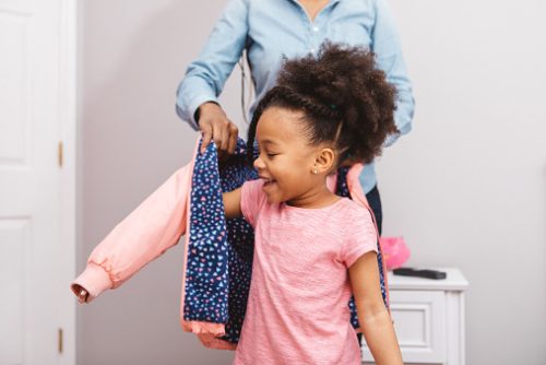 Little girl putting on her jacket to head out.