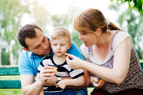 Mother and father are trying to feed their 3 year old boy in the park that refuses to eat. Genuine emotions, real family.